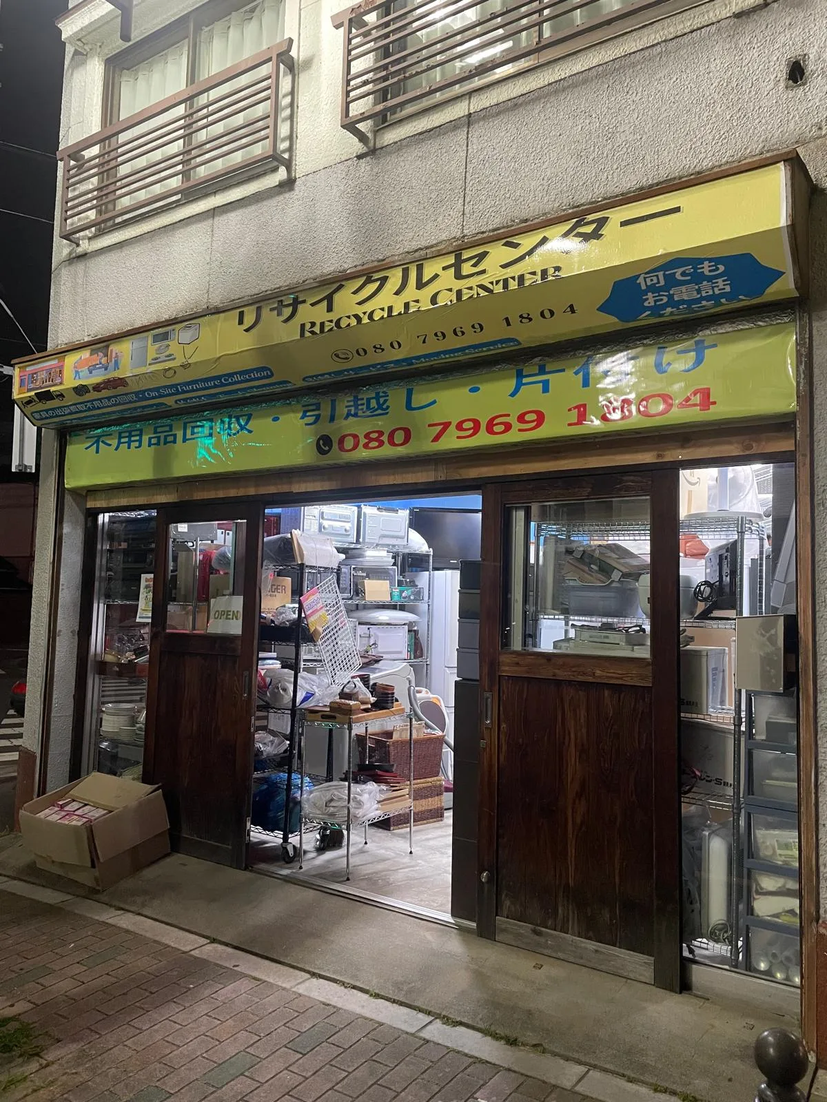 東京都北区豊島にあるリサイクルセンターの店舗外観。夜間の看板に店名と電話番号が掲げられている